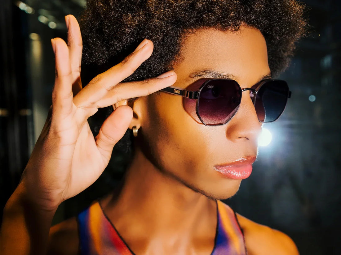 Mujer con gafas de sol OWEИ de montura oscura, sujetando una patilla.